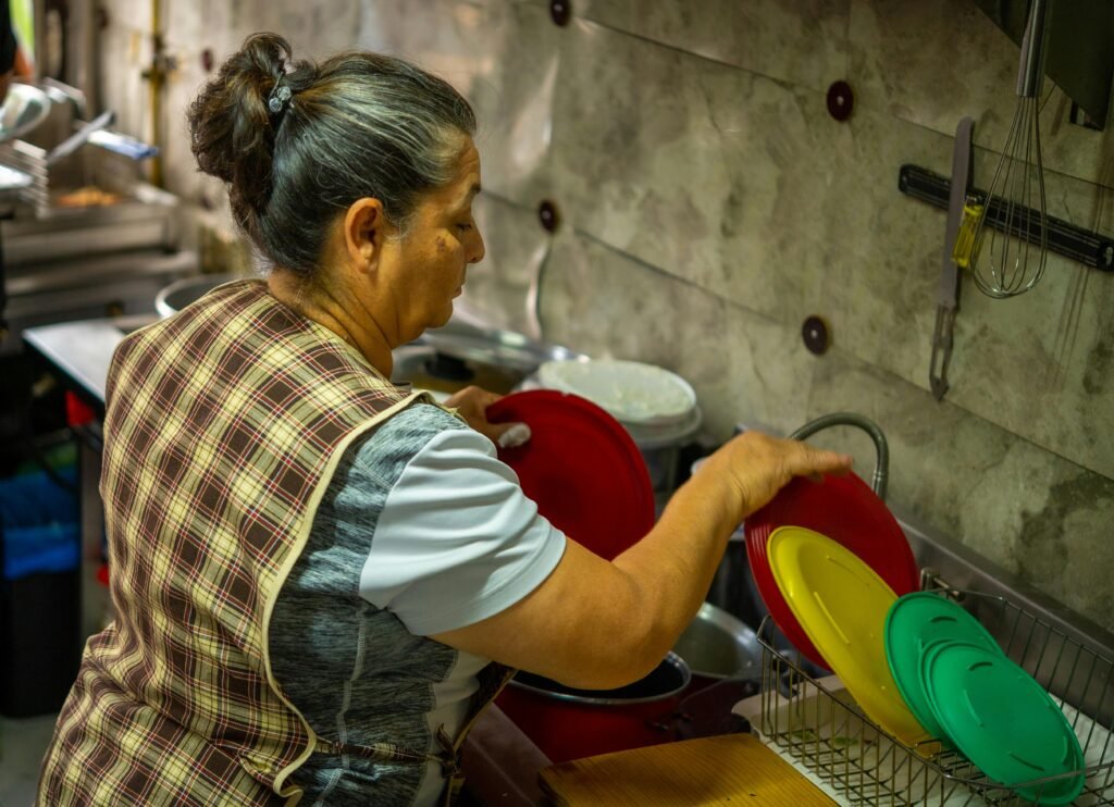 Senior woman washing colorful dishes in a kitchen, showcasing everyday domestic chores with vibrant colors.
