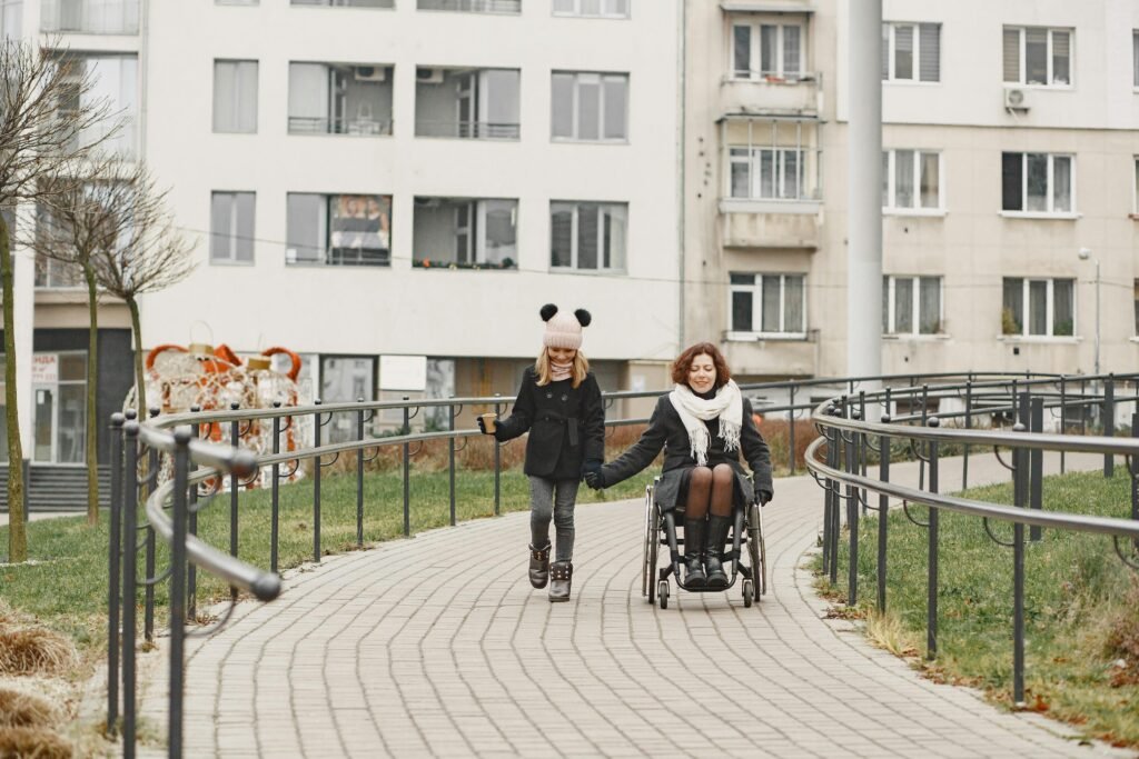 A heartwarming scene of a woman in a wheelchair holding hands with a girl outdoors on a pathway.
