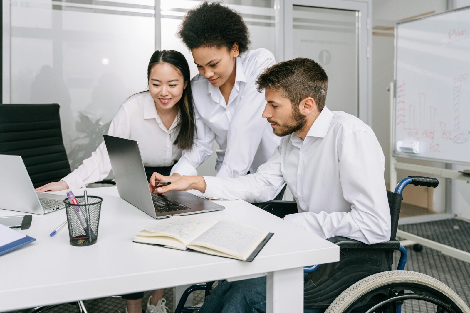 Diverse coworkers in a modern office collaborate on laptops, showcasing teamwork and inclusivity.